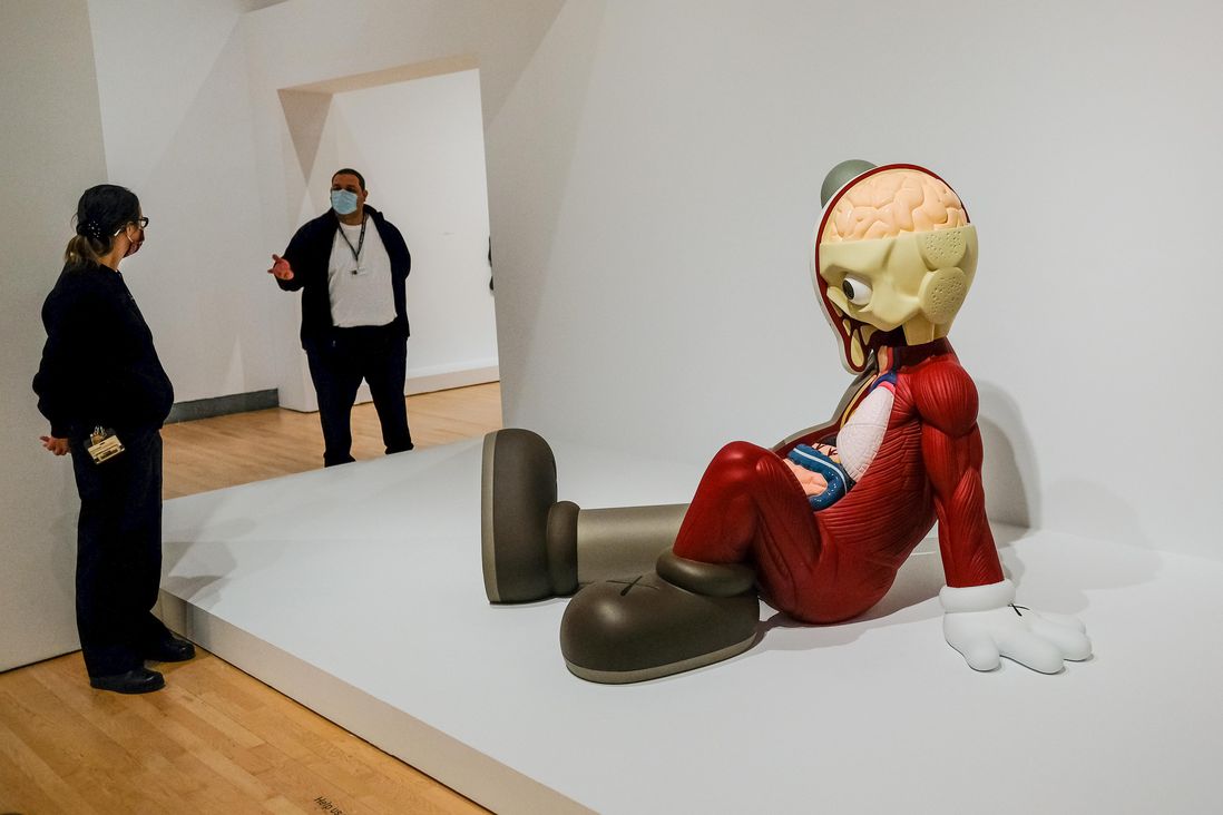 Sculpture of figure sitting on floor. Inside the KAWS exhibit at Brooklyn Museum